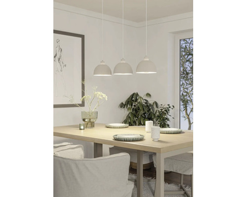 Dreiflammige Pendelleuchte über einem Esstisch aus Holz. Hell eingerichtetes Esszimmer mit Geschirr, Vase und großer Zimmerpflanze.