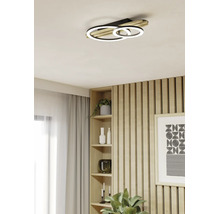 Moderne LED-Deckenleuchte in Ringform mit Holzelementen in einem hellen Wohnraum mit Holzlamellenwand und Regal.
