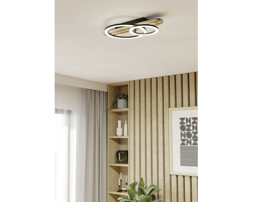 Moderne LED-Deckenleuchte in Ringform mit Holzelementen in einem hellen Wohnraum mit Holzlamellenwand und Regal.