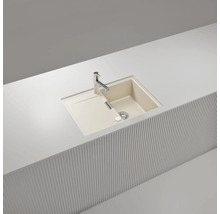 Beige Einbauspüle aus Quarzkomposit mit einem Becken, Abtropffläche und Armatur, eingebaut in eine weiße Arbeitsplatte.