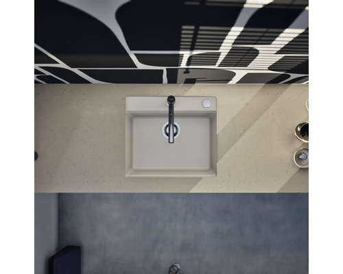 Moderne Küchenspüle mit Einhebelmischer in der Draufsicht auf einer Arbeitsplatte in Steinoptik vor einer gemusterten Wand.