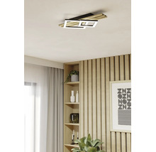 Moderne LED-Deckenleuchte in einem hellen Wohnraum mit einer Wand aus Holzlamellen, einem Einbauregal und hellen Vorhängen.