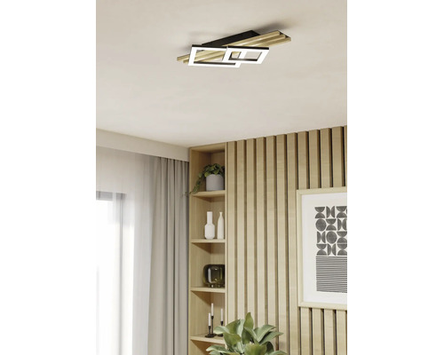 Moderne LED-Deckenleuchte in einem hellen Wohnraum mit einer Wand aus Holzlamellen, einem Einbauregal und hellen Vorhängen.