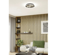 Helles Wohnzimmer mit Akustikpaneelen aus Holz an der Wand, einem weißen Sofa und einer modernen Deckenleuchte mit Holzlamellen.