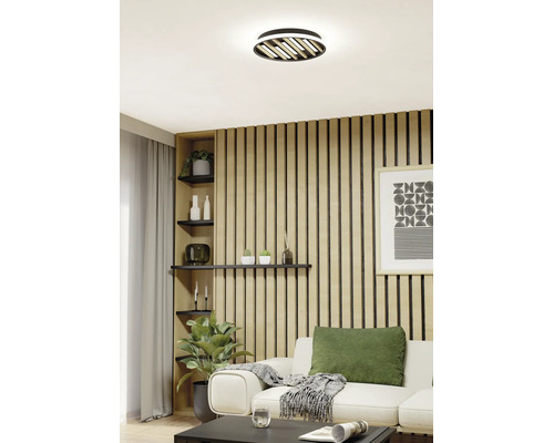 Helles Wohnzimmer mit Akustikpaneelen aus Holz an der Wand, einem weißen Sofa und einer modernen Deckenleuchte mit Holzlamellen.
