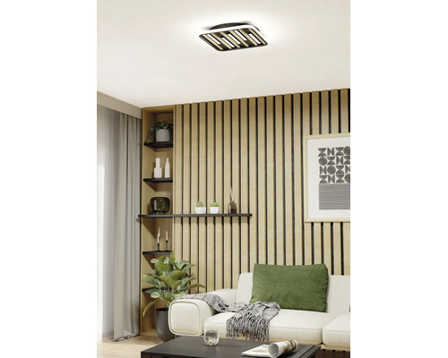 Moderne LED Deckenleuchte in quadratischer Form mit Elementen in Holzoptik in einem hellen Wohnzimmer mit Holzpaneelwand.