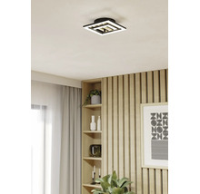 Moderne quadratische LED-Deckenleuchte mit geometrischem Design in einem hellen Raum mit Holzlamellenwand und eingebautem Regal.