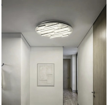 Moderne, helle Flurszene mit einer großen, strukturierten runden LED-Deckenleuchte mit mehreren Lichtstäben an einer weißen Decke.