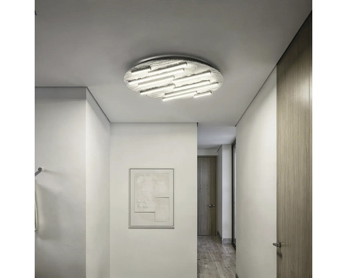 Moderne, helle Flurszene mit einer großen, strukturierten runden LED-Deckenleuchte mit mehreren Lichtstäben an einer weißen Decke.