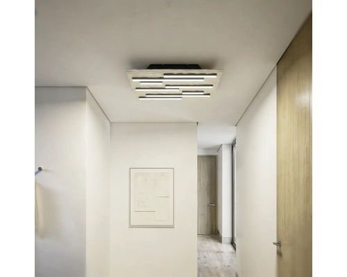Moderne LED-Deckenleuchte mit mehreren versetzt angeordneten Lichtstäben in einem hellen, minimalistischen Flur mit weißen Wänden.