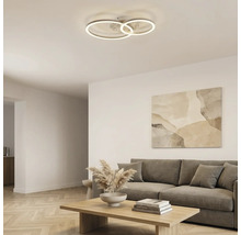 Moderne LED-Deckenleuchte mit drei ineinandergreifenden Ringen in einem hellen, organisierten Wohnzimmer mit grauem Sofa und hölzernem Couchtisch.