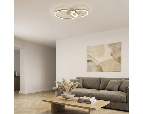 Moderne LED-Deckenleuchte mit drei ineinandergreifenden Ringen in einem hellen, organisierten Wohnzimmer mit grauem Sofa und hölzernem Couchtisch.