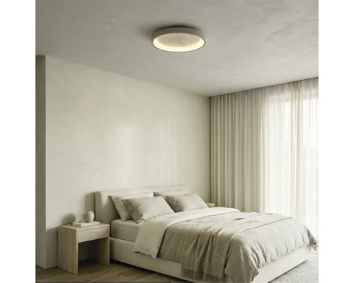Runde LED-Deckenleuchte in einem hellen Schlafzimmer mit gepolstertem Bett, Holz-Nachttisch und Vorhängen.
