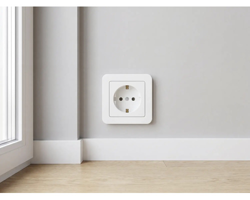 Moderne weiße Schutzkontakt-Steckdose aus Kunststoff an einer Wand über einer weißen Sockelleiste und hellem Holzboden in einem hellen Raum.