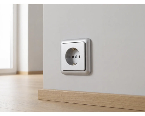Silberfarbene Schutzkontakt-Steckdose an einer hellen Wand über einer Holzfußleiste montiert.