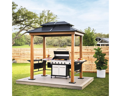 Moderner Grillpavillon aus Holz mit zweistufigem Stahldach, Seitenablagen und einem darunter stehenden Gasgrill in einem hellen Garten.