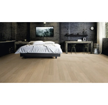 Heller Parkettboden in modernem Schlafzimmer mit dunklen Wänden in Betonoptik, weißem Bett und Holztisch.