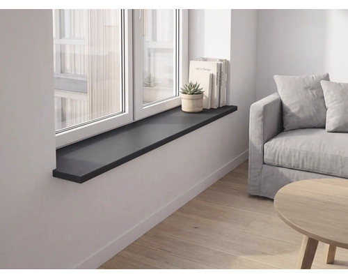 Schwarze Fensterbank in einem modernen, hellen Wohnzimmer mit Sofa, Holzboden, Büchern und einer Pflanze auf dem Sims.