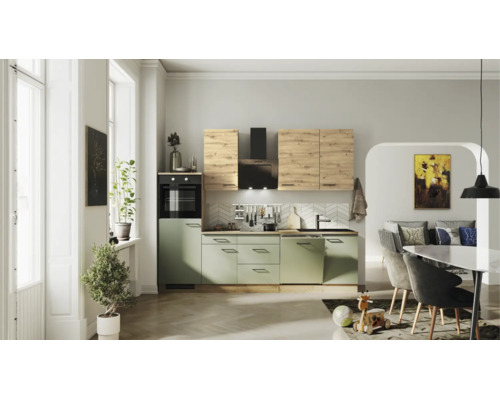 Moderne Küchenzeile mit salbeigrünen Unterschränken, Oberschränken in heller Holzoptik, schwarzem Backofen und Dunstabzugshaube in hellem Wohnraum.