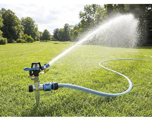 Impulsregner mit Erdspieß auf einem Rasen, angeschlossen an einen Gartenschlauch, sprüht einen weiten Wasserstrahl zur Gartenbewässerung.