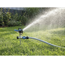 Impulsregner mit Erdspieß auf einer Rasenfläche, angeschlossen an einen Gartenschlauch, sprüht Wasser in einem weiten Strahl.