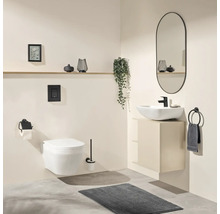 Modernes Badezimmer mit wandhängendem WC, weißem Aufsatzwaschbecken auf beigem Unterschrank, schwarzer Armatur, ovalem Spiegel und grauer Matte.