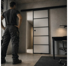 Moderne Glasschiebetür im Industrie-Design mit schwarzem Metallrahmen und satiniertem Glas in einem minimalistisch eingerichteten Arbeitszimmer.