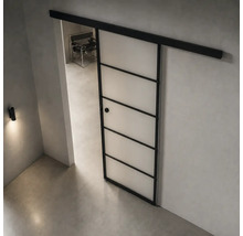 Moderne industrielle Schiebetür mit schwarzem Metallrahmen und satinierten Glasfeldern an einer schwarzen Laufschiene in einem minimalistischen Raum.