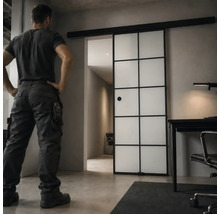 Schiebetür im Industriedesign mit schwarzem Metallrahmen und Glaseinsätzen in einem modern eingerichteten Raum mit Schreibtisch.