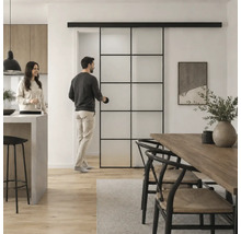 Moderne Glasschiebetür im Industrial Style mit schwarzem Metallrahmen in einem hellen Wohn- und Essbereich mit Holztisch und Personen.