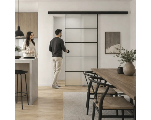 Moderne Glasschiebetür im Industrial Style mit schwarzem Metallrahmen in einem hellen Wohn- und Essbereich mit Holztisch und Personen.