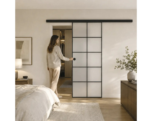 Moderne Schiebetür mit schwarzem Metallrahmen und Milchglas-Elementen in einem hellen Schlafzimmer mit begehbarem Kleiderschrank.