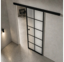 Moderne, helle Raumgestaltung mit einer Schiebetür im Industriedesign aus schwarzem Metall und Milchglas in Gitteroptik auf einem Betonboden.