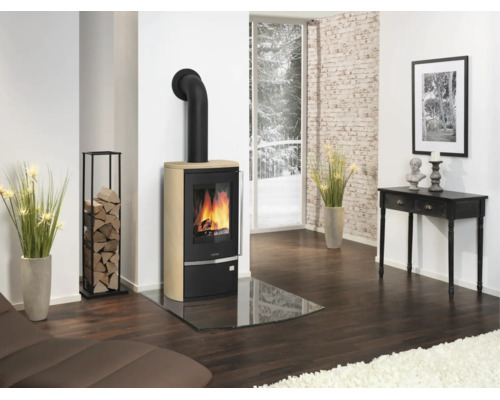 Moderner Kaminofen mit Sandsteinverkleidung und Glasbodenplatte in einem hellen Wohnzimmer mit dunklem Holzboden und Kaminholzregal.