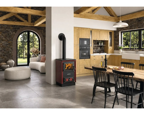 Rustikale, helle Küche mit Holzherd, Steinwänden, Holzbalken an der Decke und einem Essbereich mit schwarzem Tisch und Stühlen.
