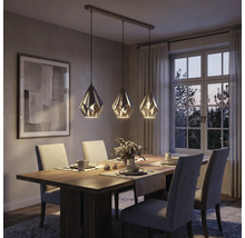 Dreiflammige Pendelleuchte mit geometrischen Metallschirmen über einem Holzesstisch in einem modern eingerichteten Esszimmer.