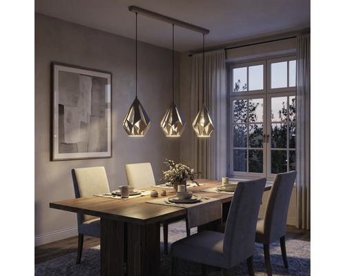 Dreiflammige Pendelleuchte mit geometrischen Metallschirmen über einem Holzesstisch in einem modern eingerichteten Esszimmer.
