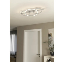 Moderne LED-Deckenleuchte mit vier ineinandergreifenden Ringen in einem hellen Wohnraum mit weißer Tür und minimalistischer Einrichtung.