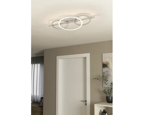Moderne LED-Deckenleuchte mit vier ineinandergreifenden Ringen in einem hellen Wohnraum mit weißer Tür und minimalistischer Einrichtung.