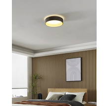 Helles, modernes Schlafzimmer mit einer runden Deckenleuchte, Wandpaneelen aus Holzlatten, einem Bett und einem Fenster mit Jalousien.