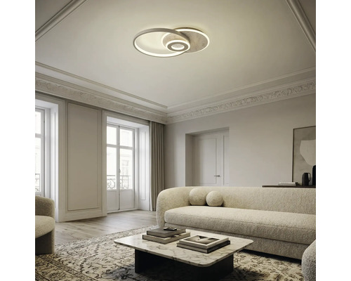 Moderne LED-Deckenleuchte mit ineinandergreifenden Ringen in einem hellen, elegant eingerichteten Wohnzimmer mit Sofa und Couchtisch.
