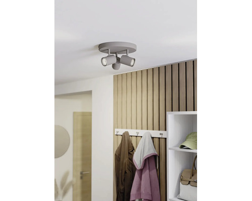 Grauer dreiflammiger Deckenstrahler an einer weißen Decke in einem modernen Flur mit Holzlamellenwand und Garderobe.