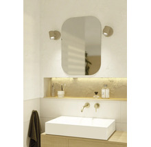 Modernes, helles Badezimmer mit weißem Aufsatzwaschbecken, Holzunterschrank, Wandarmatur, abgerundetem Spiegel und zwei Wandleuchten.