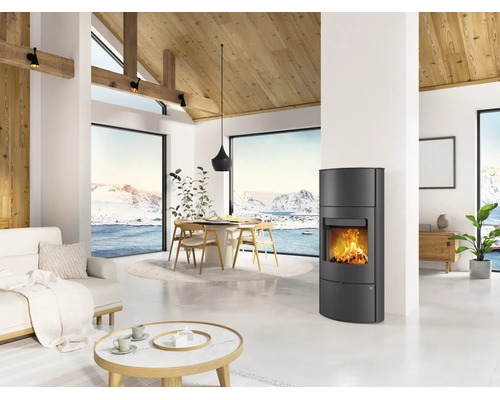 Moderner Kaminofen in einem hellen Wohnzimmer mit hohen Decken, Holzgebälk und Panoramafenstern mit Blick auf eine Schneelandschaft.