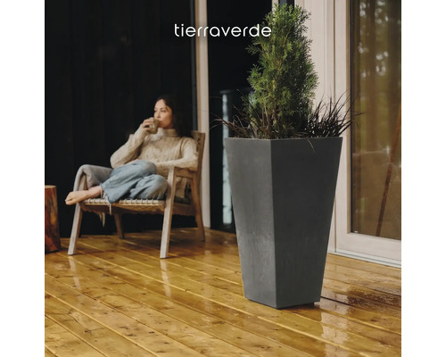 Hoher, konischer Pflanzkübel in Anthrazit auf einer Holzterrasse neben einer sitzenden Person. Tierra Verde Logo.