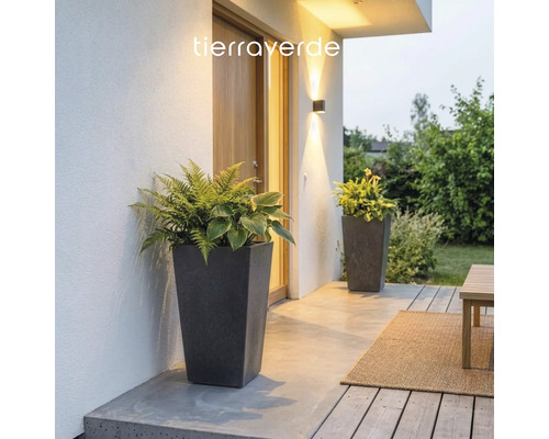 Zwei hohe konische Pflanzgefäße in Steinoptik mit Farnen und Hostas auf einer modern beleuchteten Terrasse. Tierraverde Logo.