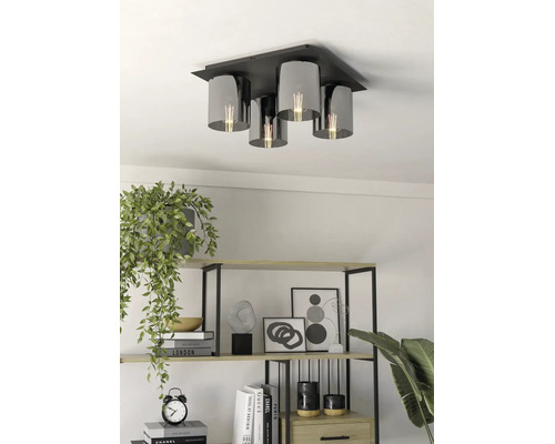 Vierflammige Deckenleuchte mit schwarzer Metallbasis und zylindrischen Schirmen aus Rauchglas in einem hellen Wohnraum mit Regal.