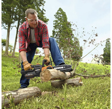 Mann mit Schutzbrille und Handschuhen beim Zersägen eines Holzstamms mit einer Worx Akku-Kettensäge im Freien.