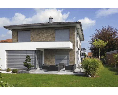 Modernes zweistöckiges Haus mit Außenjalousien an Fenstern und Terrasse, Klinkerfassade sowie Garten mit Lounge-Möbeln und Rasenfläche.