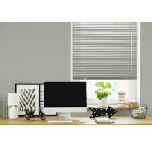 Eine horizontale Jalousie an einem Fenster über einem modern eingerichteten Schreibtisch mit Monitor, Lampe und Dekoration im Arbeitszimmer.